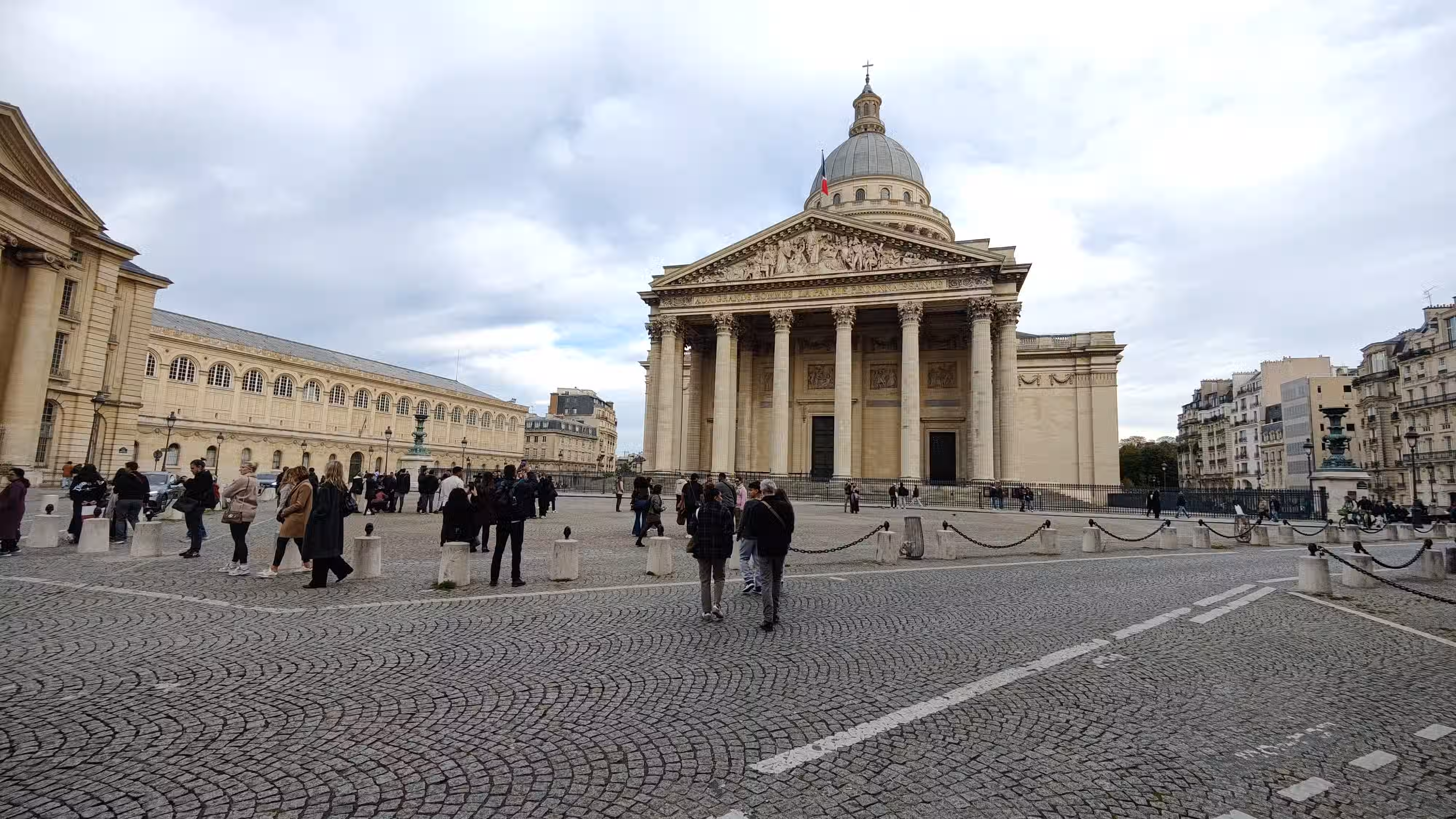 A building with a dome shaped structure on top. Closer to camera, roads can be seen. In the background is blue colored cloudy sky.