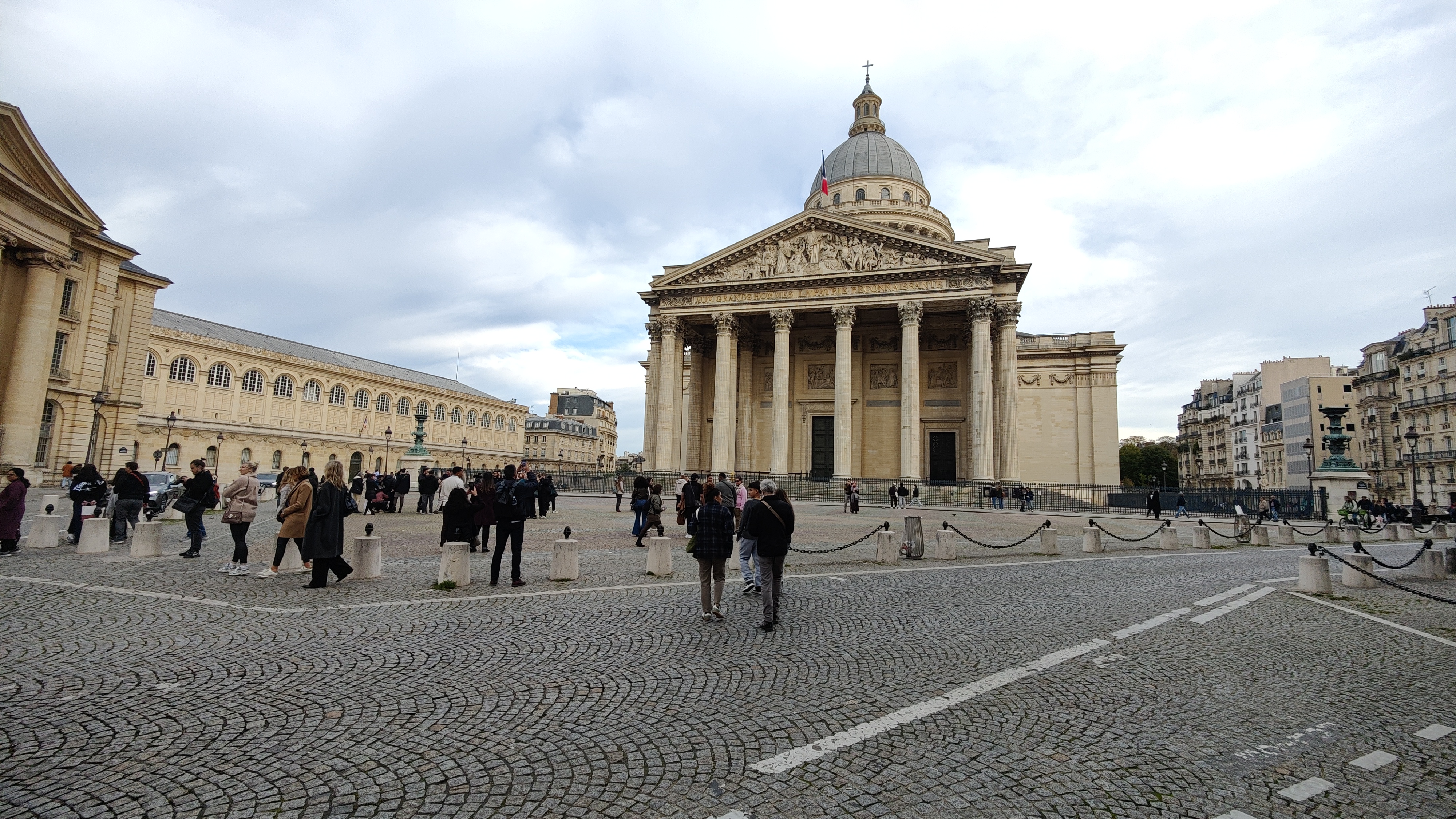 A building with a dome shaped structure on top. Closer to camera, roads can be seen. In the background is blue colored cloudy sky.